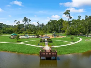 Vista panorámica del parque central con juegos infantiles, área de chapoteadero y muelle frente al lago en la comunidad Lakes at Black Oak, Magnolia, Texas.